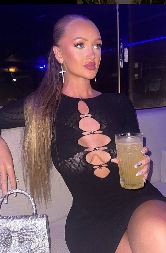@christinalegreid sitter i en bar mens hun har på seg en sexy svart kjole og holder en drink i hånden.