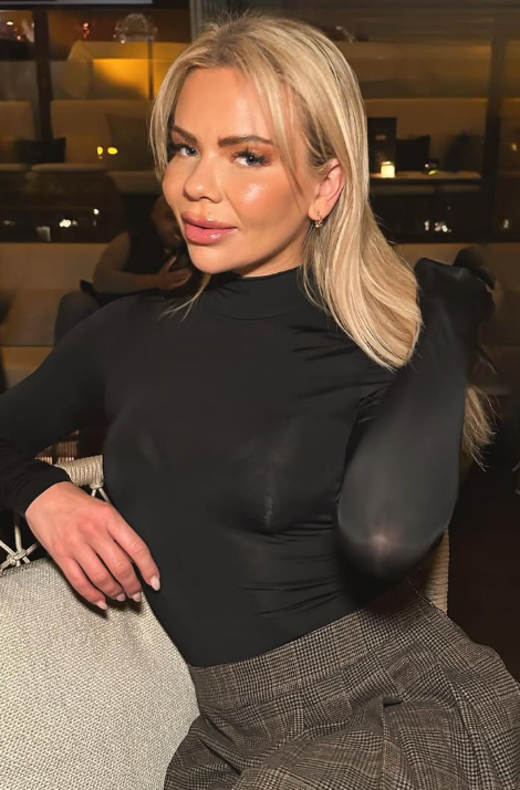 @julianyland sitter på en stol og har på seg en sexy svart tett topp og et grått skjørt.