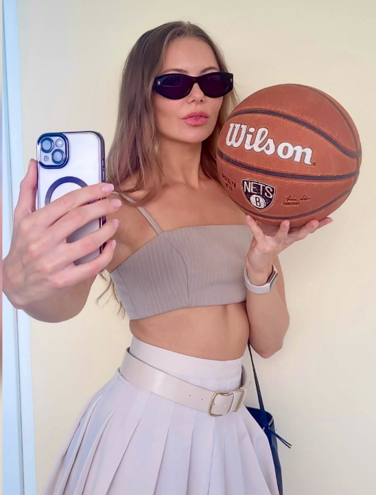 Nora North tar et bilde mens hun holder en basketball i hånden og er kledd i en askegrå crop-topp og hvitt skjørt.