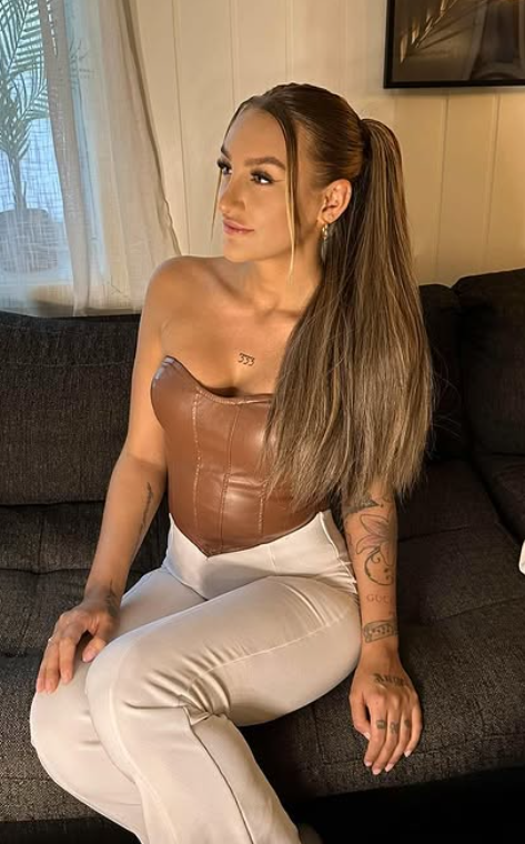 Julie Linnea Hovelsen sitter i en sofa kledd i en sexy brun ermeløs topp og hvite bukser.