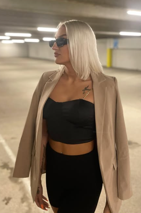 Julie Linnea Hovelsen tar et bilde mens hun er kledd i en sexy svart crop-kjole og svarte shorts med en brun jakke på skuldrene.