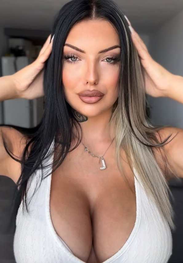 Lisa Johansen tar et bilde mens hun er kledd i en sexy hvit, utringet topp med hendene pÄ hodet.