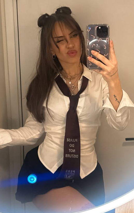 Siv Nerdal tar et bilde i en sexy hvit skjorte, slips og svart skjørt mens hun holder telefonen i hånden.