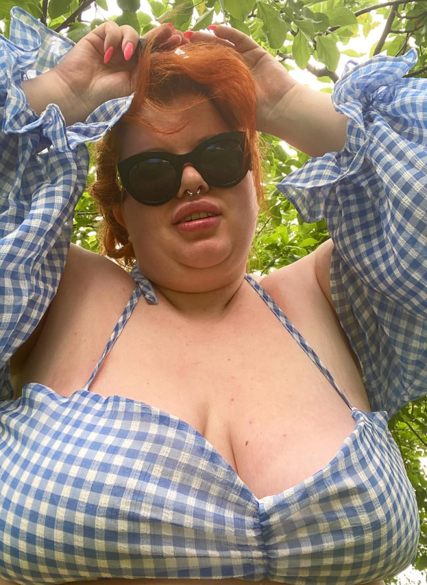 Ginger Minx tar et bilde i skogen og har på seg et sexy blått antrekk med hendene på hodet.