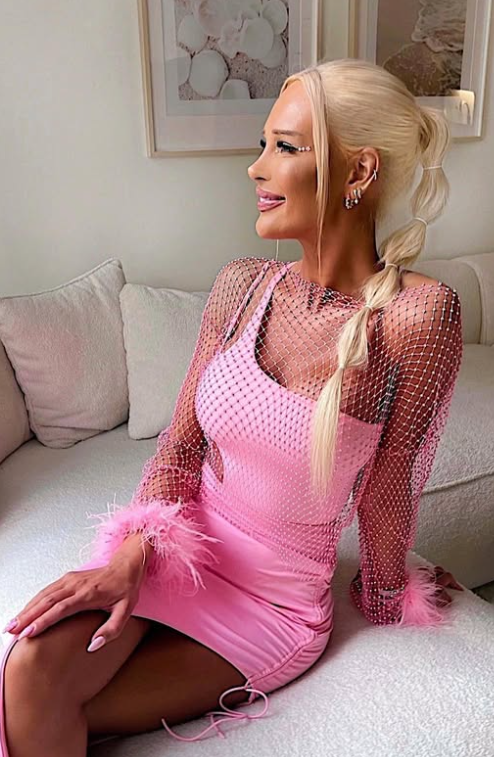 Julie Olivia sitter på sofaen og kledd i et sexy rosa antrekk.