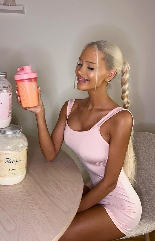 Julie Olivia tar et bilde mens hun er kledd i et sexy rosa antrekk og holder en kopp i hendene.